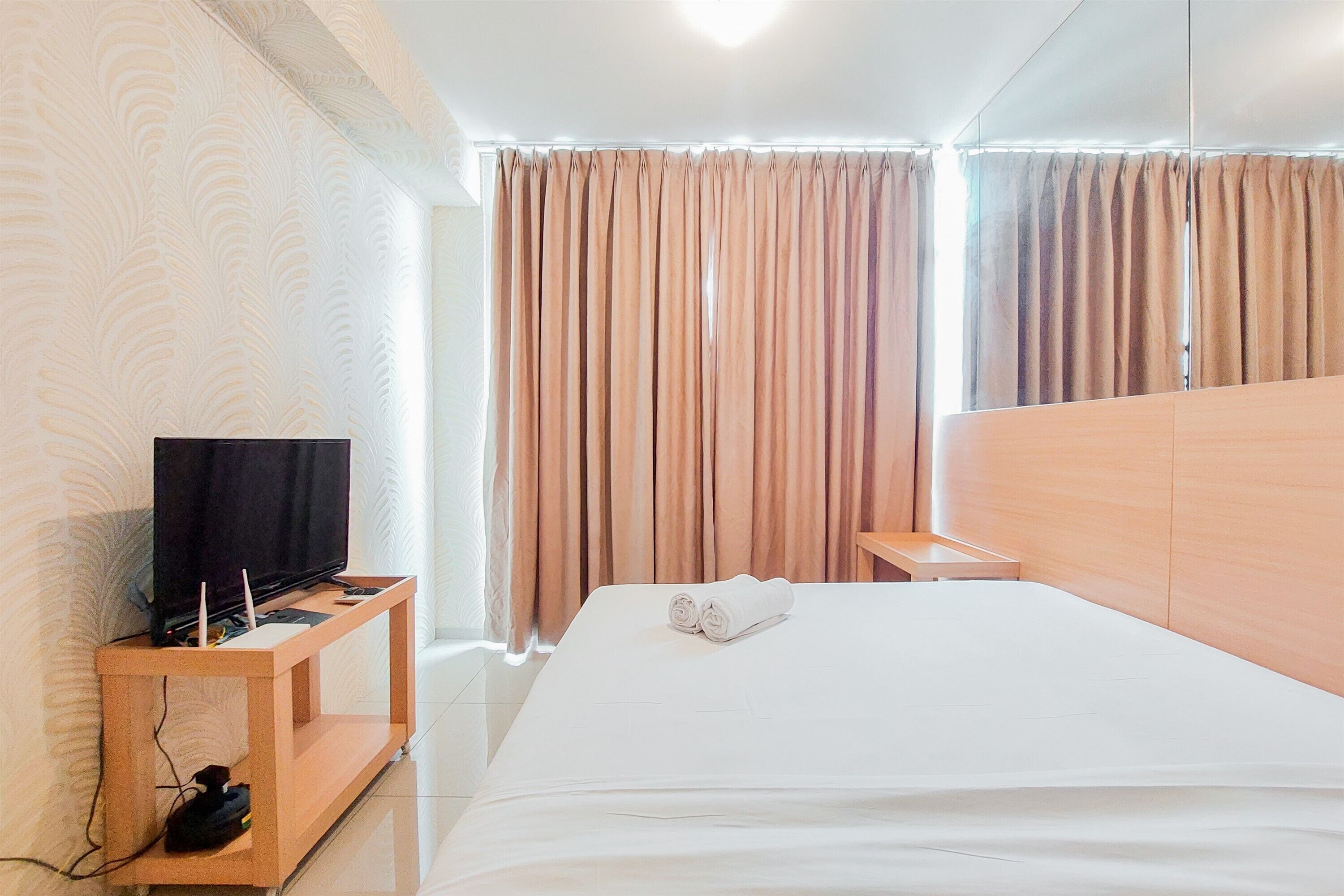 A hotel room with a bed, a TV on a wooden stand, and curtains.