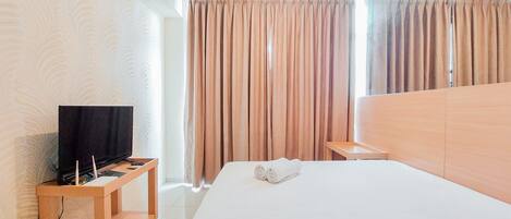 A hotel room with a bed, a TV on a wooden stand, and curtains.