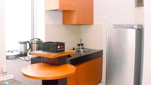 A compact kitchen with a stainless steel refrigerator, a microwave, a kettle, and a coffee maker on the countertop. - Comfort Studio At Marina Ancol Apartment (Jakarta)