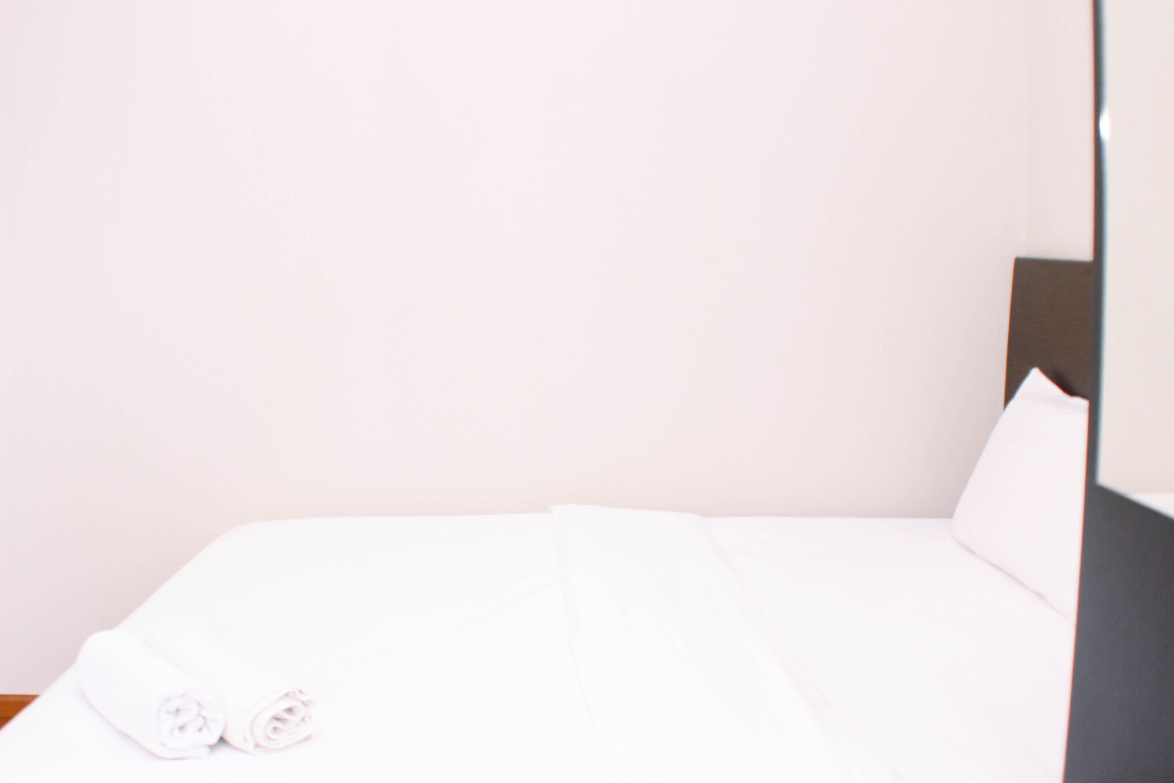 A neatly made bed with white linens and two rolled towels on the left side.