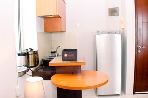 A compact kitchen with a microwave, stove, and a travel bag on a small table.