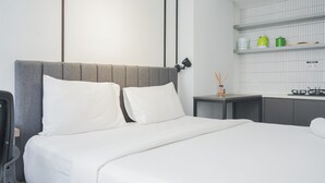 A modern hotel room with a bed, a small bedside table, and a kitchenette area. - Warm And Simply Studio Room At Urbantown Serpong Apartment (South Tangerang)