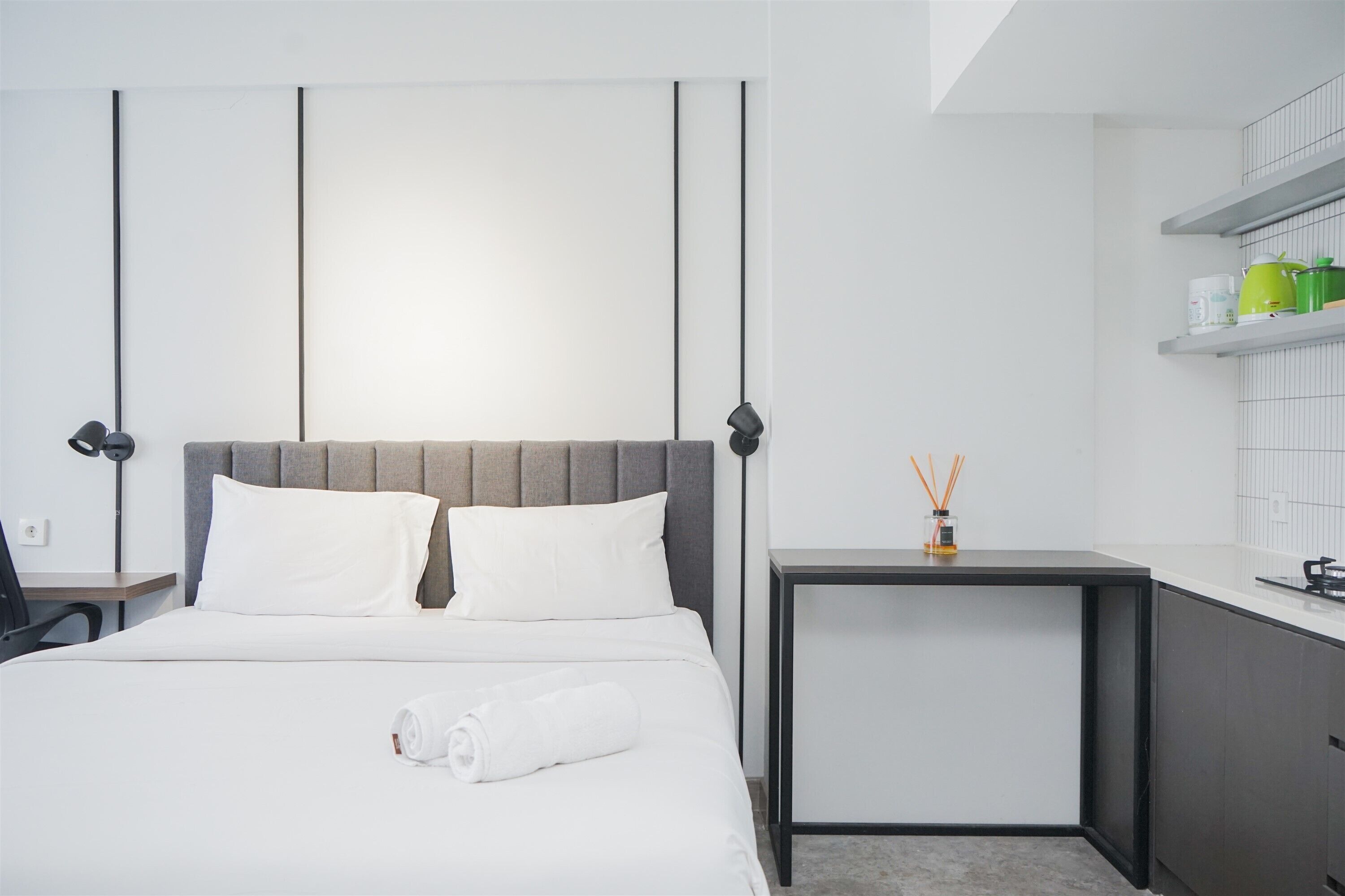 A modern hotel room with a large bed, a desk, and a small kitchenette.