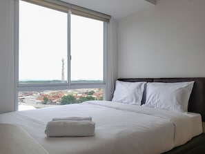Quarto de hotel com uma janela ampla, cama com roupa de cama branca e vista para a paisagem urbana.