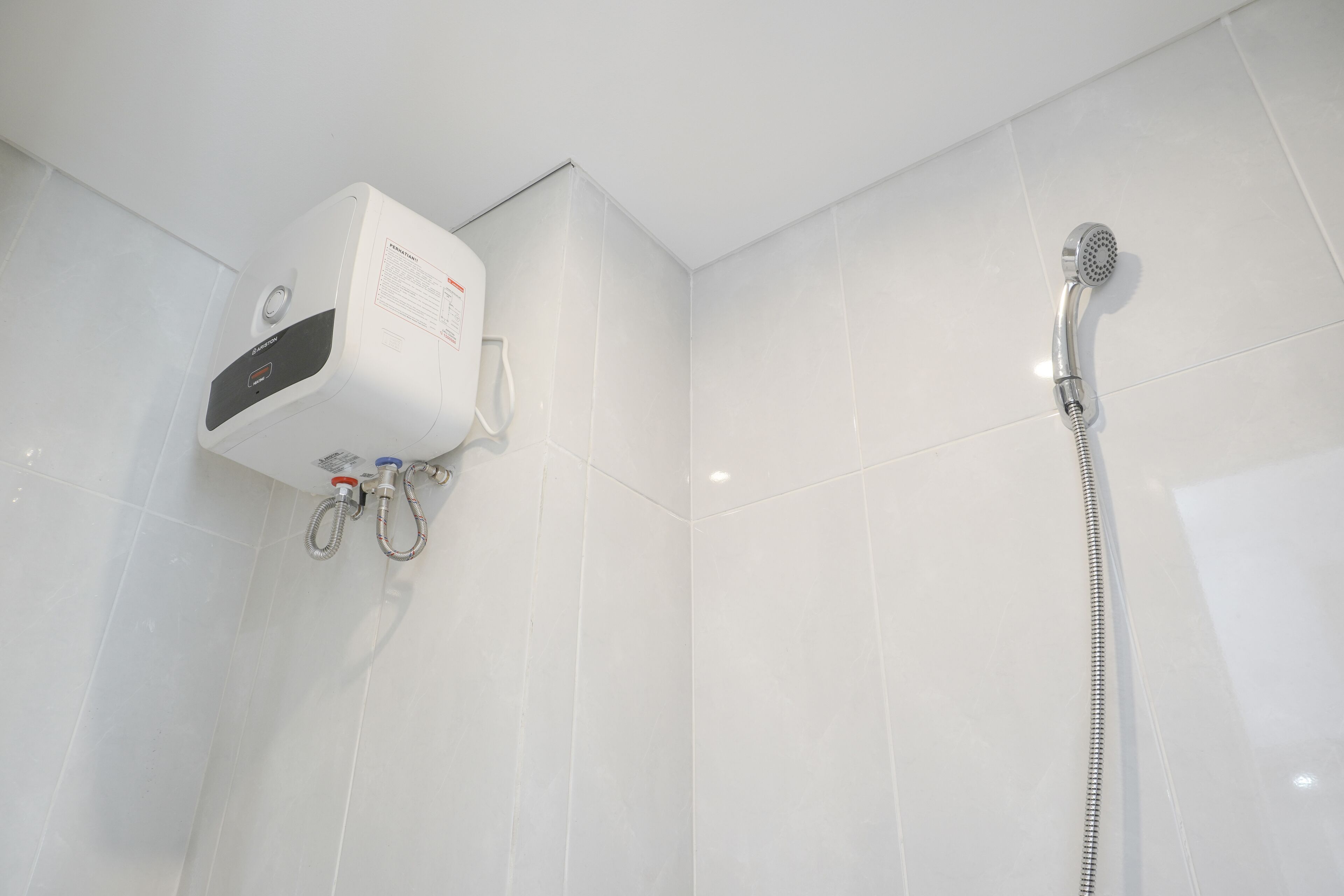 A modern bathroom with white tiles, a built-in showerhead, and a handheld shower attachment.