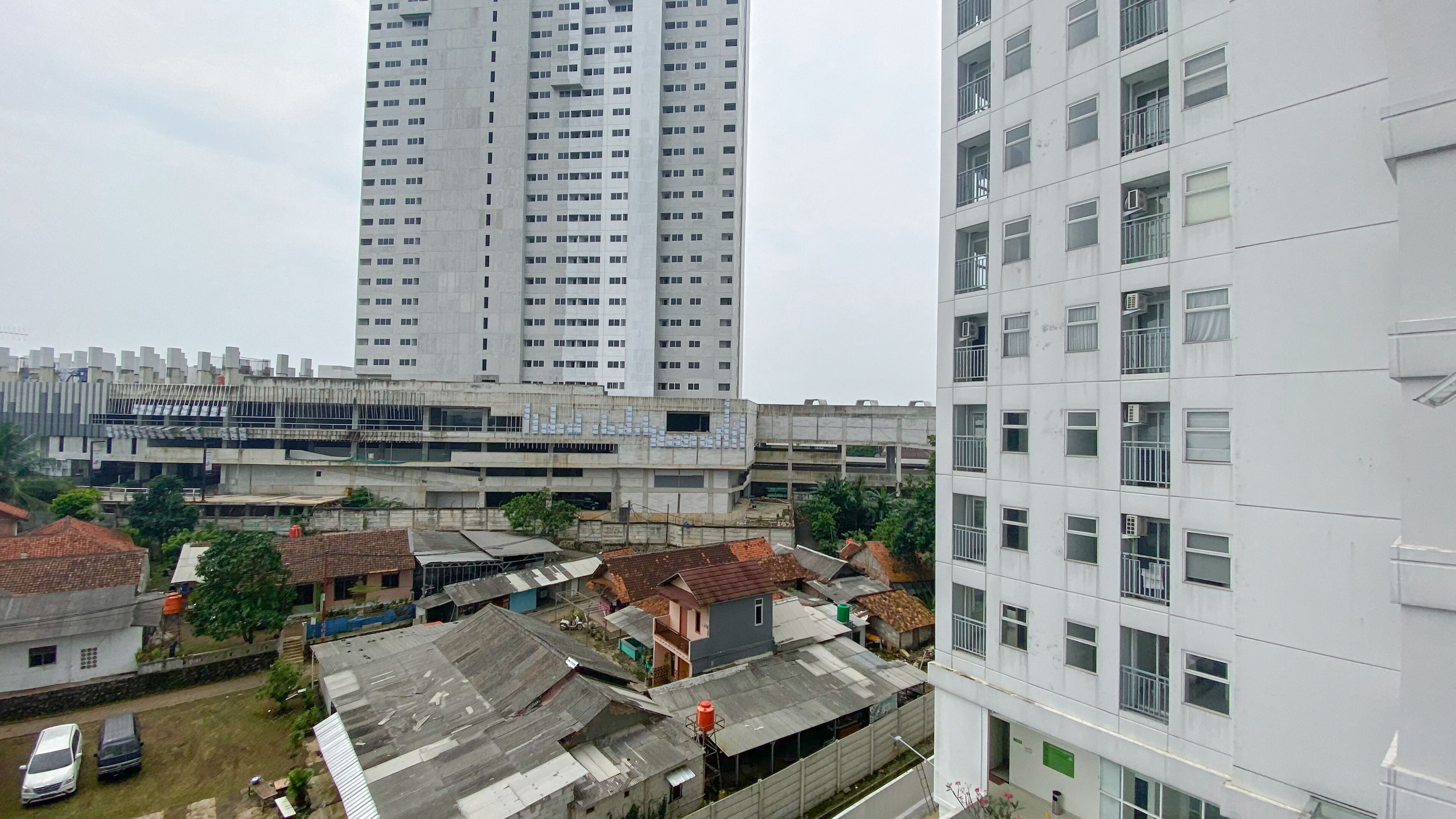 Un immeuble de grande hauteur, doté de nombreux étages et de balcons, entouré de bâtiments plus petits aux toits de styles variés.