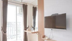 Ein Hotelzimmer mit Bett, einem an der Wand montierten Fernseher, einem kleinen Tisch mit Telefon und Flasche sowie einem Fenster mit Vorhängen.