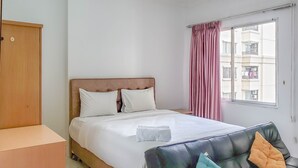 Een slaapkamer met een bed, een houten kledingkast, een raam met gordijnen en uitzicht op gebouwen.