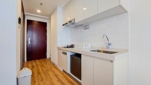 A compact kitchen with white cabinets, a stainless steel sink, and a dishwasher. - Warm And Simply Studio Apartment At Sky House Bsd (Pagedangan)