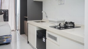A compact kitchen with a sink, stove, and a compact refrigerator. - Fully Furnished With Tidy Design Studio At Sky House Bsd Apartment (Pagedangan)