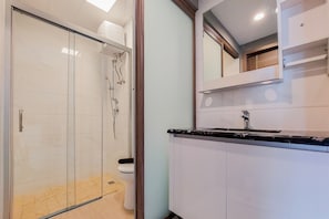 A bathroom with a glass shower enclosure, a toilet, and a sink with a mirror above it. - Relaxing 2Br At Sky House Bsd Apartment (Pagedangan)