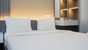 Ein modernes Hotelzimmer mit einem ordentlich bezogenen Bett, einem integrierten Schminktisch mit Spiegel und einer Wandleuchte.