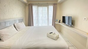 Ein Hotelzimmer mit einem großen Bett, einem Fernseher auf einem Regal und Blick auf Gebäude durch das Fenster.