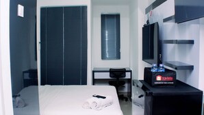 A hotel room with a bed, a desk, a chair, a TV, and a minibar. - Nice And Homey Studio At Sayana Bekasi Apartment (Bekasi)