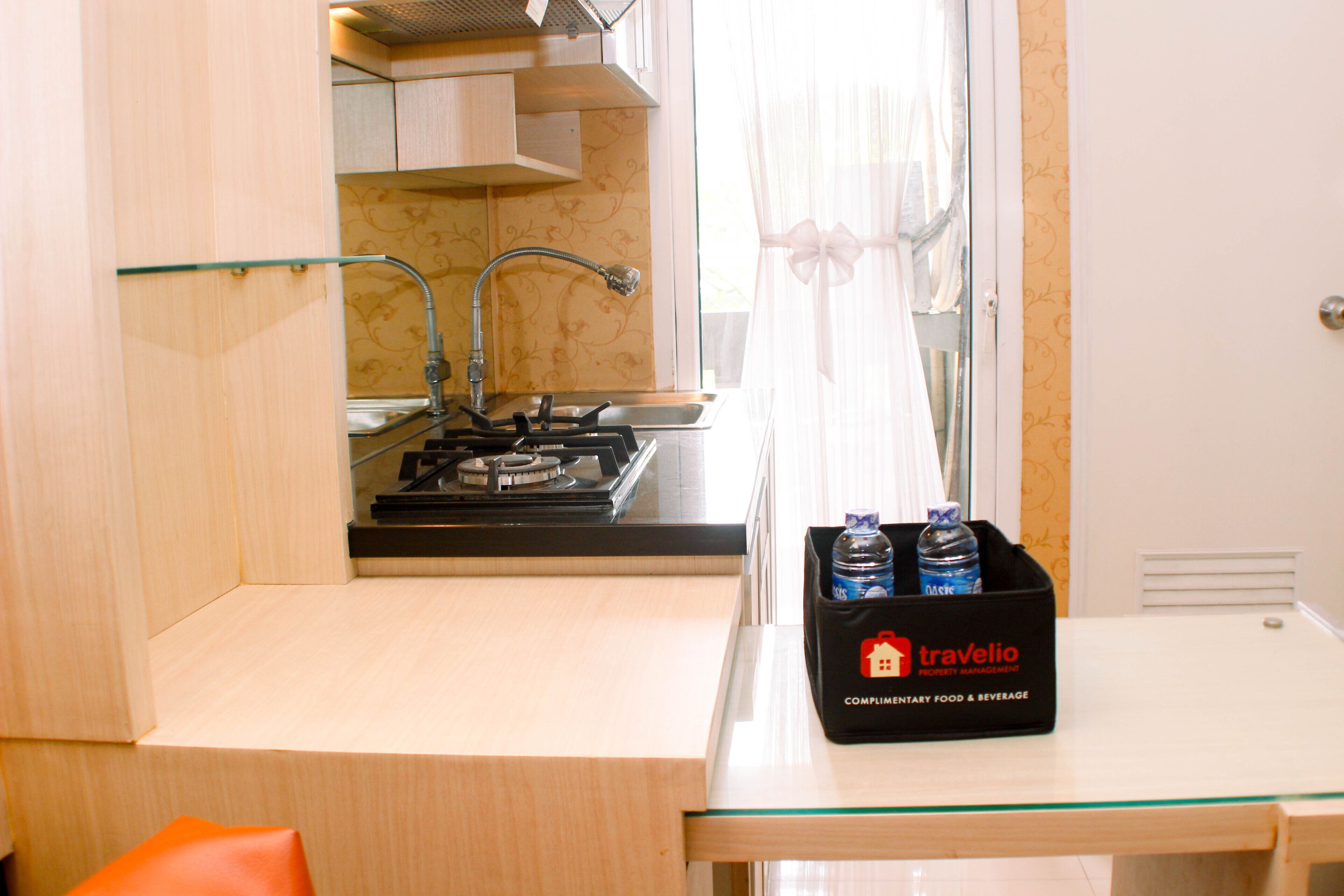 Une cuisine compacte équipée d’une cuisinière à gaz, d’un évier et d’un plan de travail en verre. Une boîte noire portant l’inscription « Travelio » est posée sur le plan de travail.