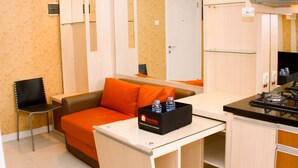 A hotel room with a sofa, a small table, a chair, a kitchen area with a stove, and a minibar. - Nice And Strategic 2Br At Green Pramuka City Apartment (Jakarta)