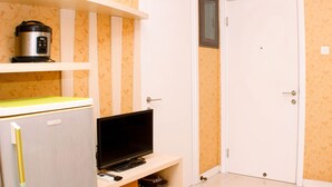 A compact room with a television on a stand, a small refrigerator, and a microwave on a shelf. - Nice And Strategic 2Br At Green Pramuka City Apartment (Jakarta)