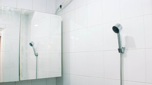 A bathroom with white tiled walls, a mirror, and a shower with a handheld showerhead. - Nice And Strategic 2Br At Green Pramuka City Apartment (Jakarta)