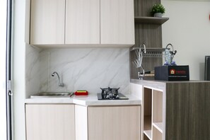 A compact kitchen with a sink, stove, and a small shelf with a plant.