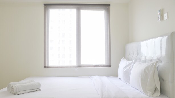 A hotel room with a large window, a neatly made bed, and a wall-mounted light switch. - Stunning And Comfy 2Br Bassura City Apartment (Jakarta)