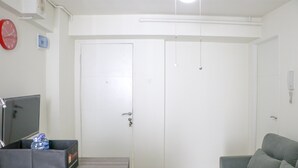 A room with a grey sofa, a television on a stand, a water bottle in a box, and a white door. - Stunning And Comfy 2Br Bassura City Apartment (Jakarta)