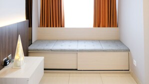 Ein modernes Zimmer mit eingebauter Sitzbank, einem Nachttisch mit Lampe und einem fenster mit Vorhängen.