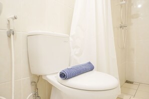 Un baño con un inodoro blanco, una ducha y una toalla sobre el asiento del inodoro.