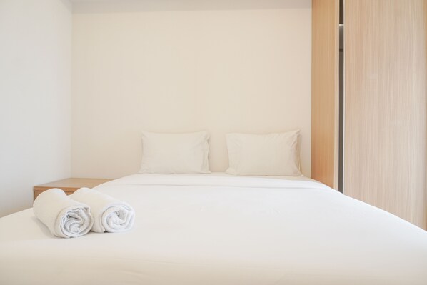 Una cama bien hecha con sábanas y almohadas blancas, una mesita de noche de madera y una puerta de madera.
