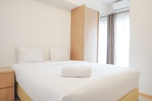 Una cama bien hecha con ropa blanca y una toalla doblada, un armario de madera y una ventana con cortinas.