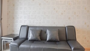 Ein modernes Wohnzimmer mit einem grauen Ledersofa, zwei passenden Kissen und einer gemusterten Tapete.