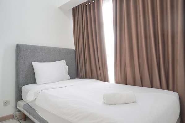 Un lit bien fait, avec du linge de lit blanc, une tête de lit grise et un oreiller blanc.