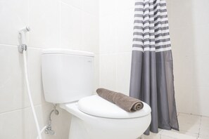 Une salle de bain avec des toilettes blanches, un rideau de douche et une serviette posée sur la lunette des toilettes.