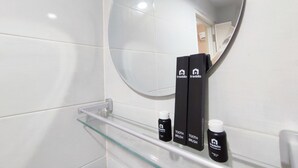 Une salle de bain avec des carreaux blancs, une étagère en verre, deux brosses à dents et un tube de dentifrice.