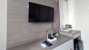 Une chambre moderne équipée d’un téléviseur à écran plat fixé au mur, d’un petit bureau avec une télécommande et d’un vase décoratif contenant des fleurs.
