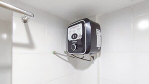 Kylpyhuone, jossa on valkoiset laatat, musta seinälle asennettu lämminvesivaraaja ja metallinen kaide.