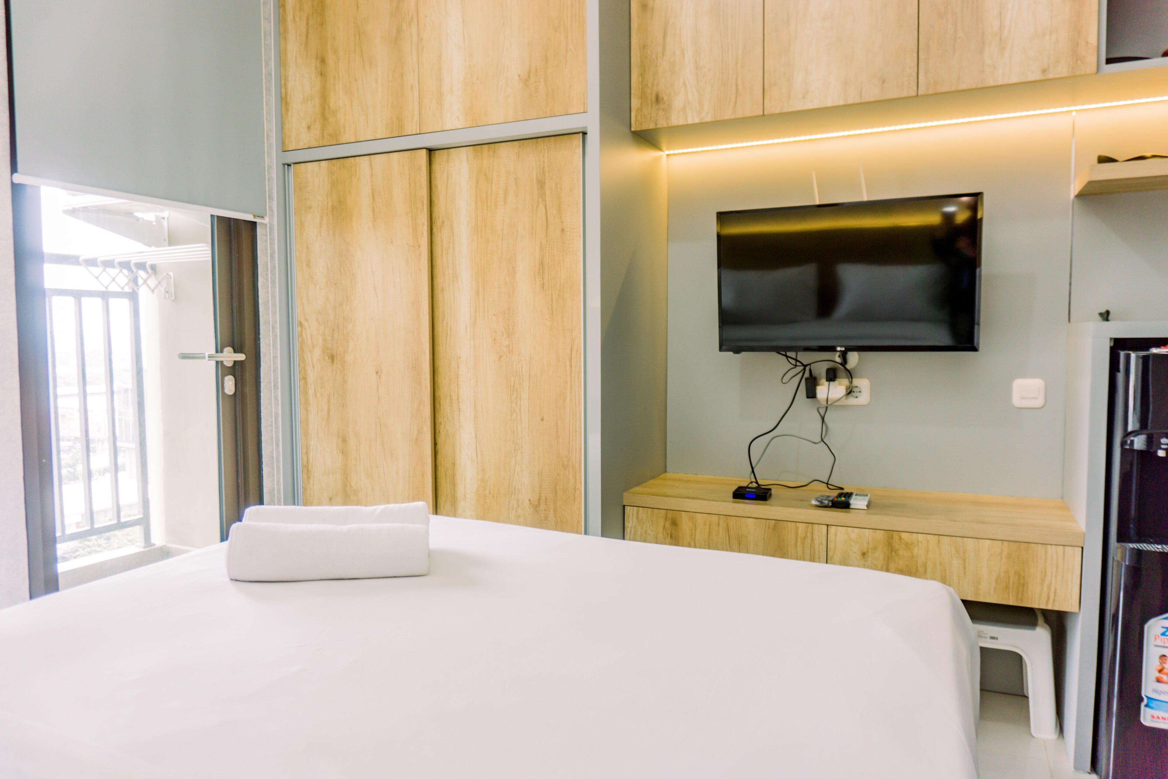 A hotel room with a bed, wooden wardrobe, a TV mounted on the wall, and a small table with a chair.
