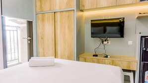 A hotel room with a bed, wooden wardrobe, a TV mounted on the wall, and a small table with a chair. - Fancy And Nice Studio Room At Transpark Bintaro Apartment (South Tangerang)