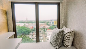 A room with a large window, a bed with pillows, and a view of a cityscape. - Fancy And Nice Studio Room At Transpark Bintaro Apartment (South Tangerang)