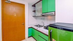 A compact kitchen with a wooden door, green cabinets, a sink, and a refrigerator. - Relaxing Studio Apartment At Margonda Residence 2 Near Ui (Depok)