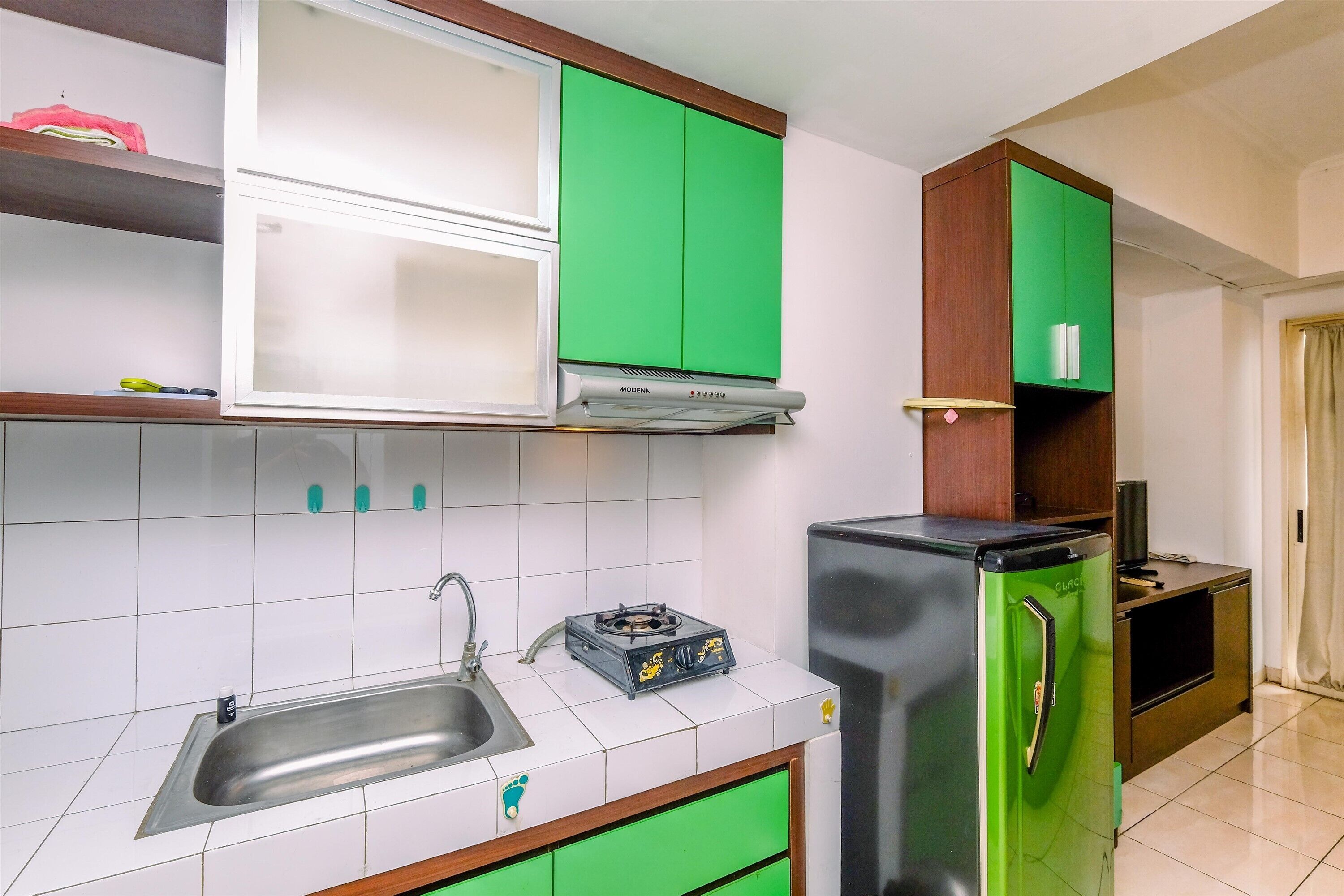 A compact kitchen with white and green cabinets, a stainless steel sink, a gas stove, and a refrigerator.