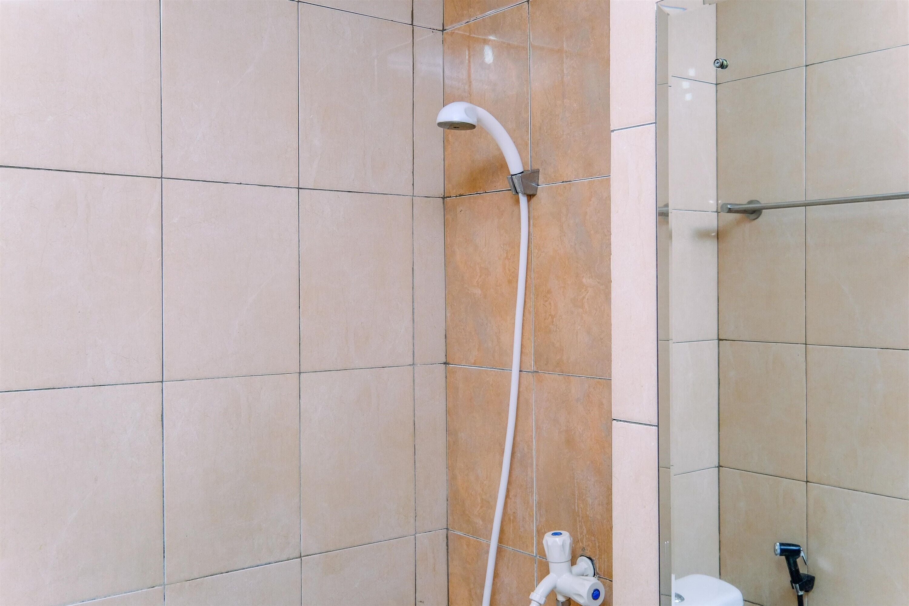 Un baño con azulejos color beige, un cabezal de ducha blanco y un inodoro a la vista.