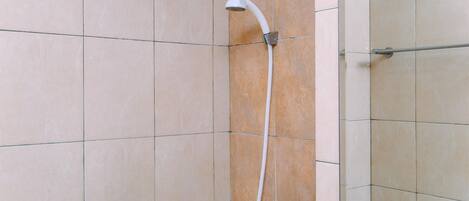 Un baño con azulejos color beige, un cabezal de ducha blanco y un inodoro a la vista.