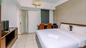 A hotel room with a bed, a desk with a chair, a television, and an air conditioning unit. - Relaxing Studio Apartment At Margonda Residence 2 Near Ui (Depok)