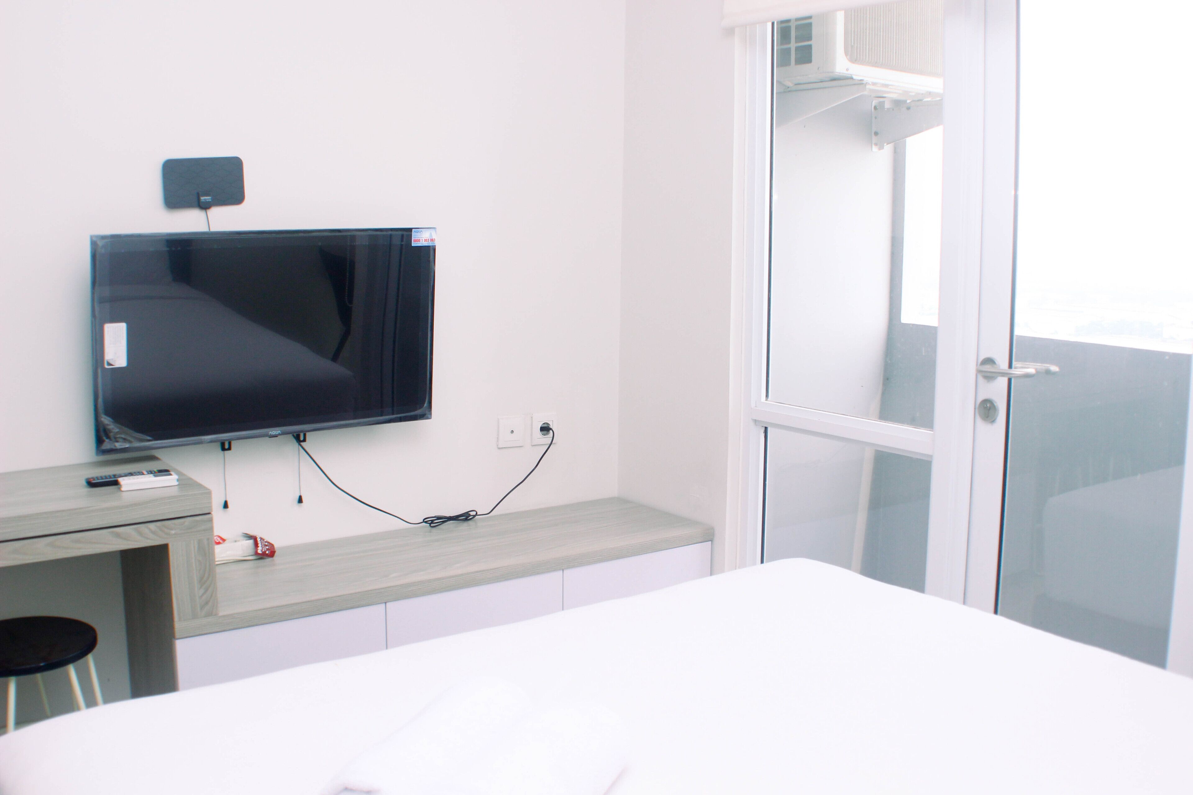 Une chambre d’hôtel moderne dotée d’un téléviseur à écran plat fixé au mur, d’un bureau en bois avec une chaise et d’une grande fenêtre offrant une vue sur la ville.
