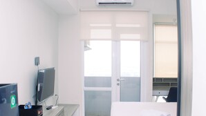 Habitación de hotel con cama, escritorio con computadora y televisor, baño con ducha y puerta que da a un balcón.