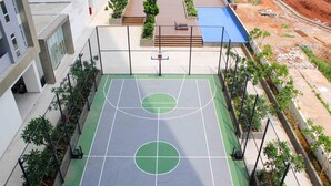 Una cancha de baloncesto al aire libre con aro, rodeada por una valla y follaje.