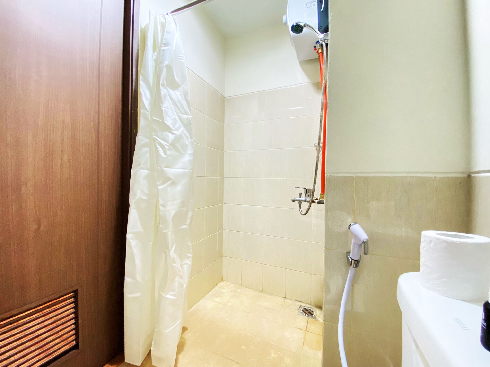 A small, enclosed shower area with a showerhead, a white curtain, and a toilet.
