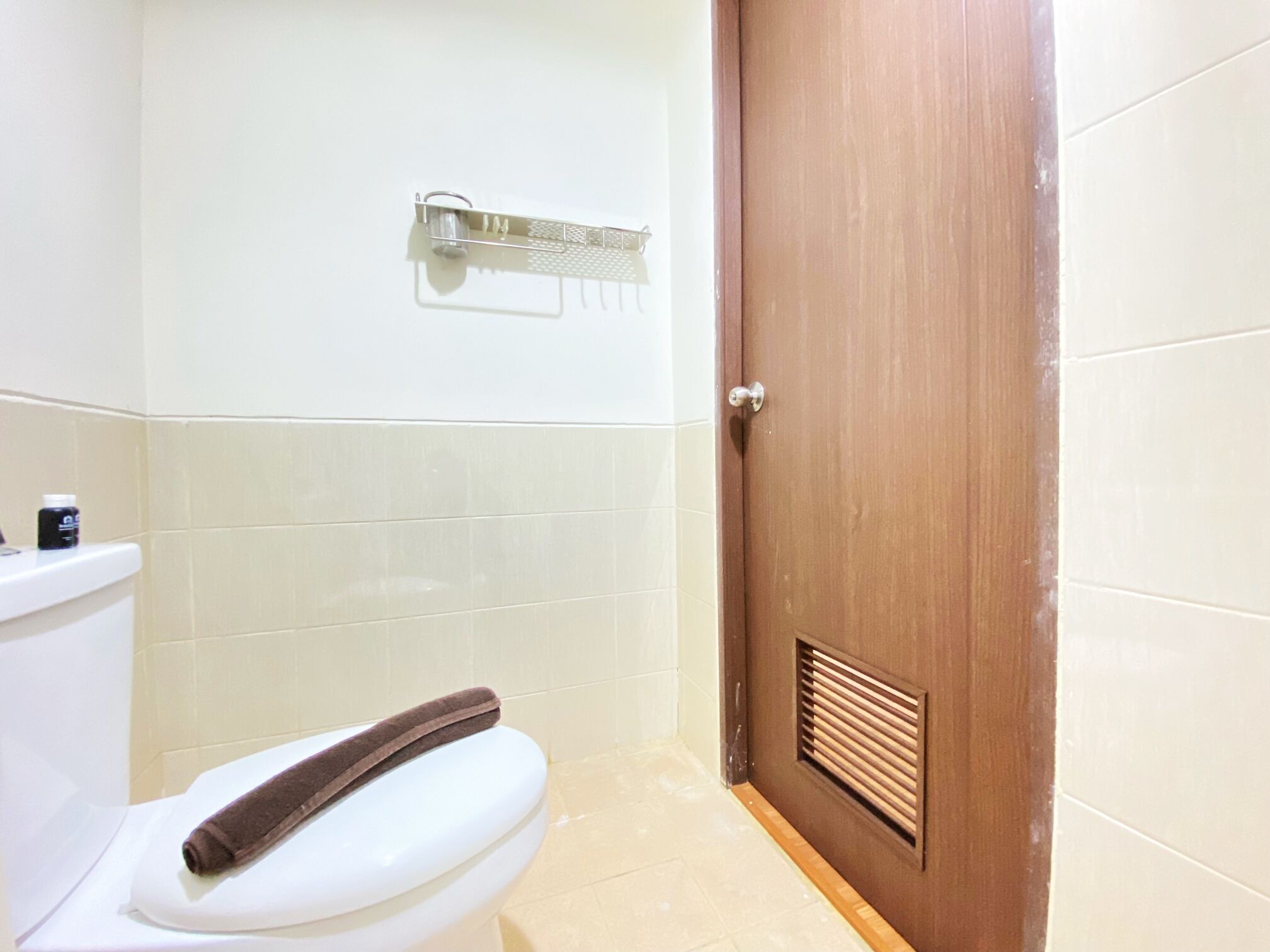 Un baño con inodoro blanco, puerta de madera y un perchero para toallas.