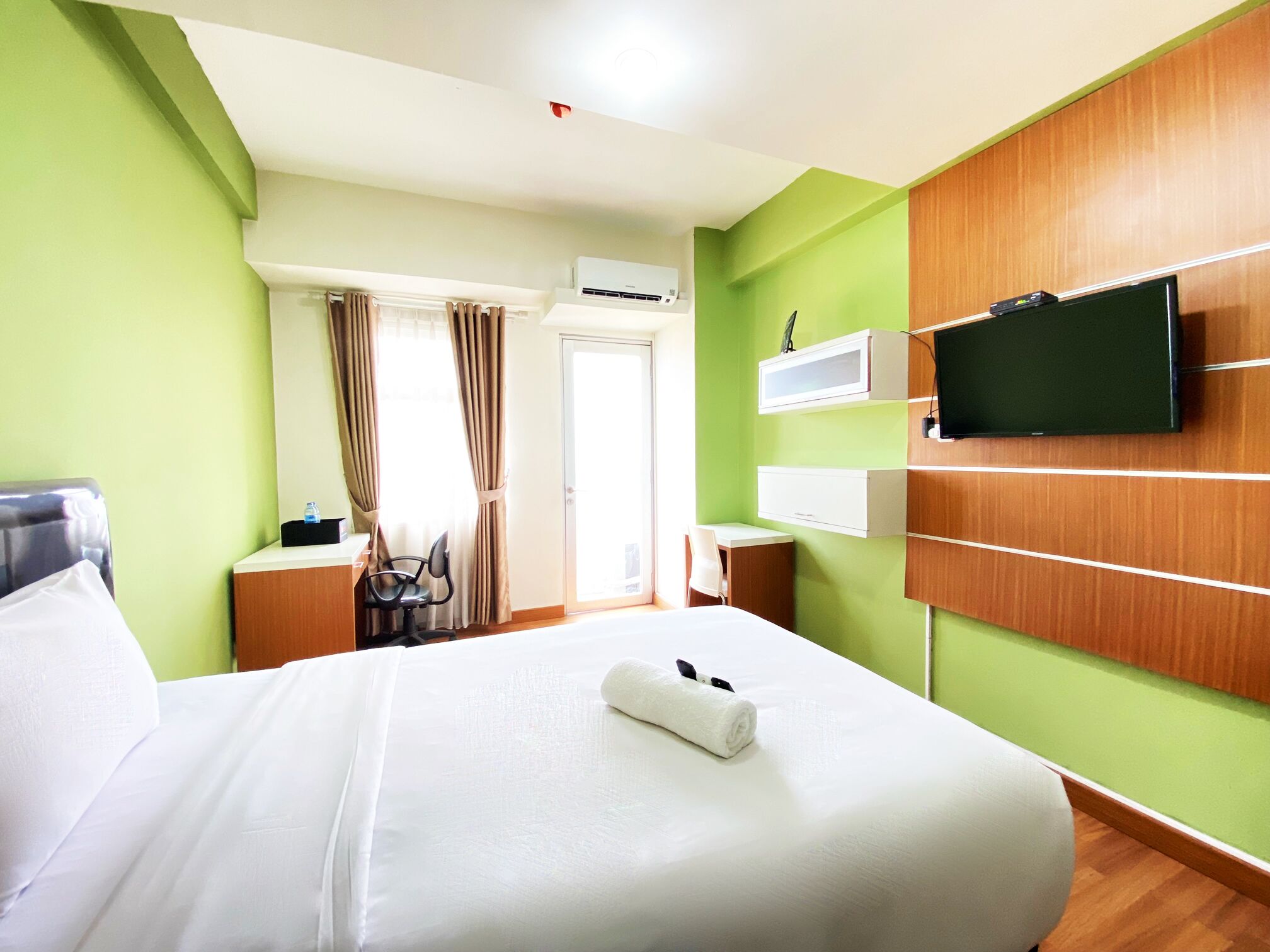 A hotel room with a bed, a desk, a chair, a television, and an air conditioning unit.