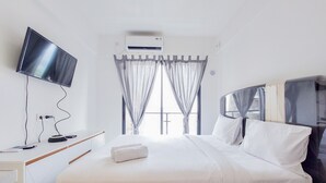 Habitación de hotel con cama, televisión montada en la pared, aire acondicionado y ventana con cortinas.